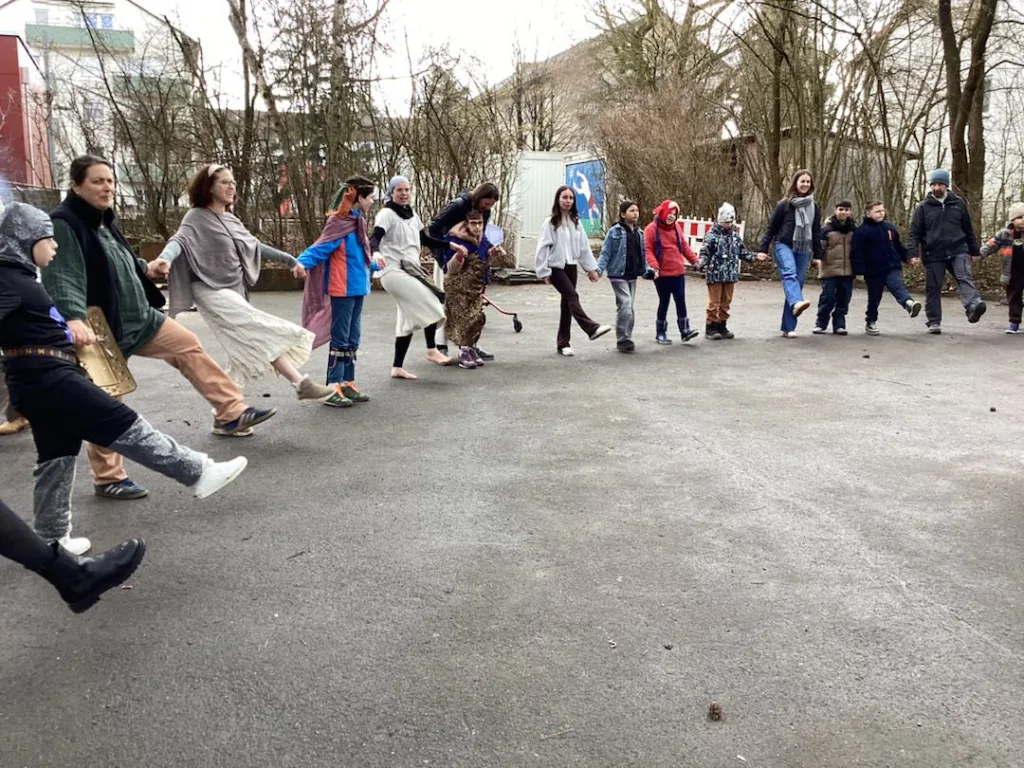 Kinder und Erwachsene tanzen einen Gruppentanz und fassen sich an den Händen.