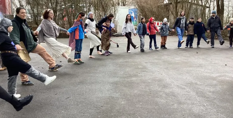 Kinder und Erwachsene tanzen einen Gruppentanz und fassen sich an den Händen.